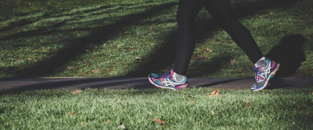 A picture of a persons legs and feet running on a path that is between two grassy areas.