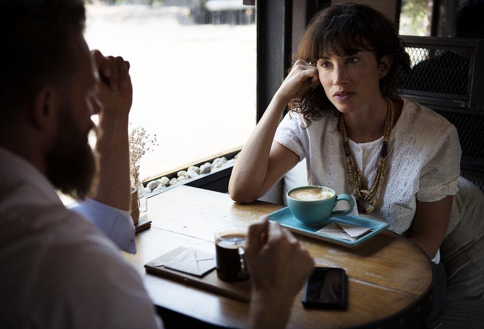 A man and a woman sitting in a café talking with a cup of coffee