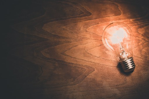 A screw cap light bulb on a wooden surface illuminating part of it.