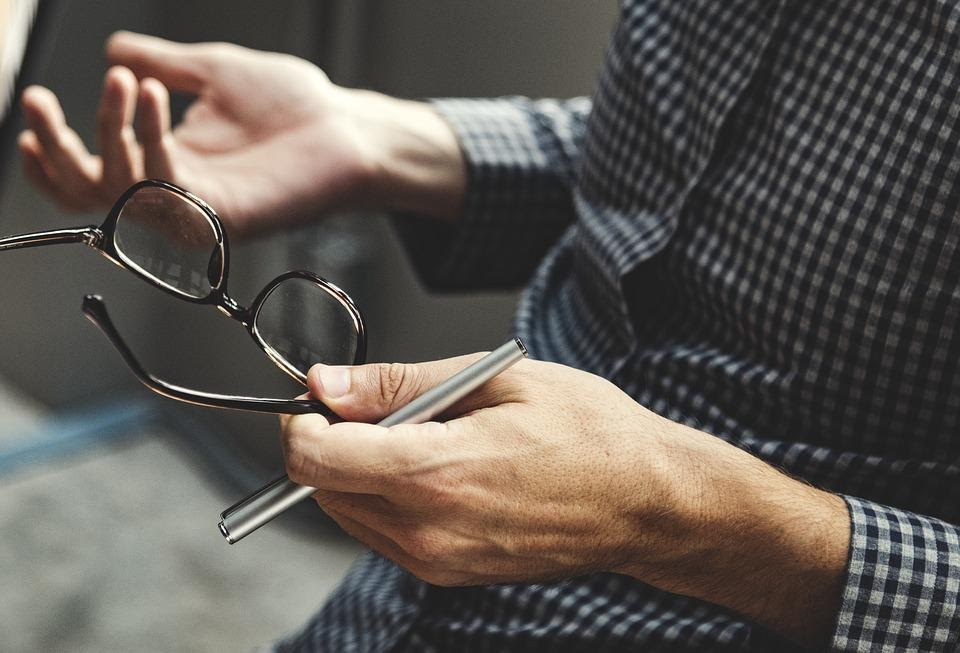 A close-up of a therapist using their hands to explain, holding some glasses and a pen