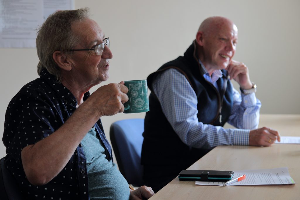 Image of two men chatting together in a classroom and looking happy.