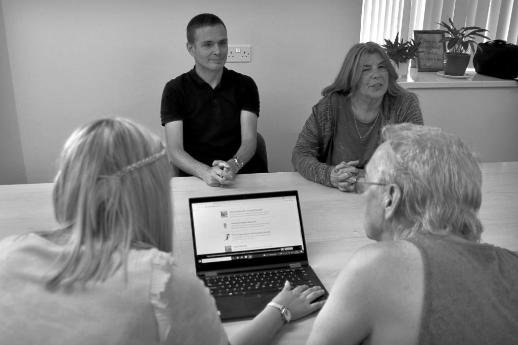 Group of students working on a laptop together in a recovery college classroom.