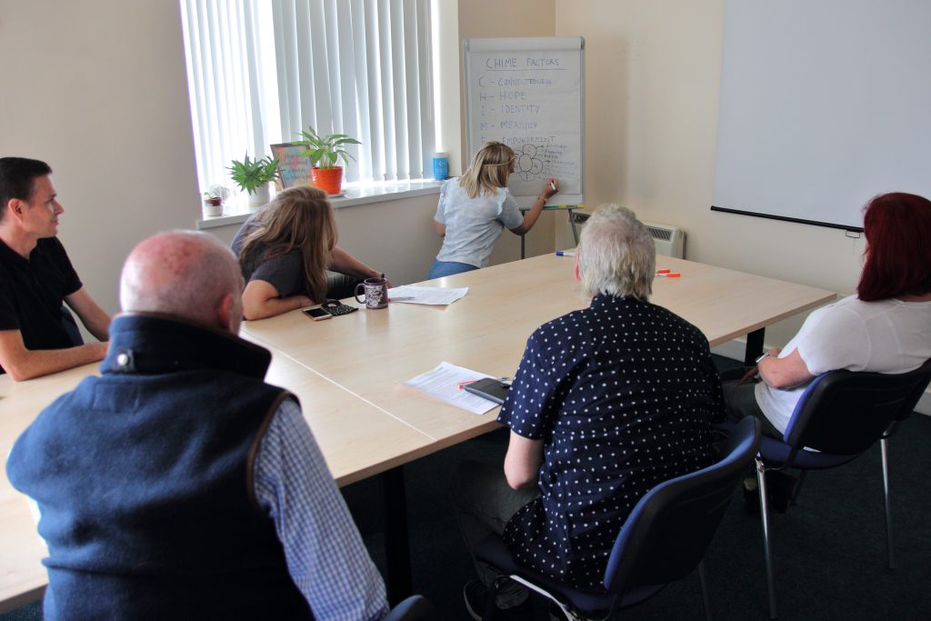 Group of men and women chatting and learning round a table in a classroom.