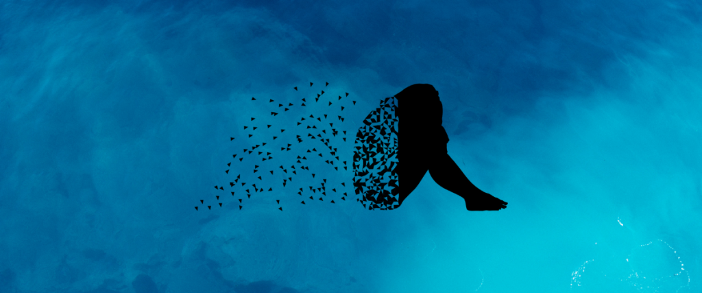 A blue liquid background with a silhouette of a person sat holding their knees with their head down, their back is disintegrating into small triangular flecks.