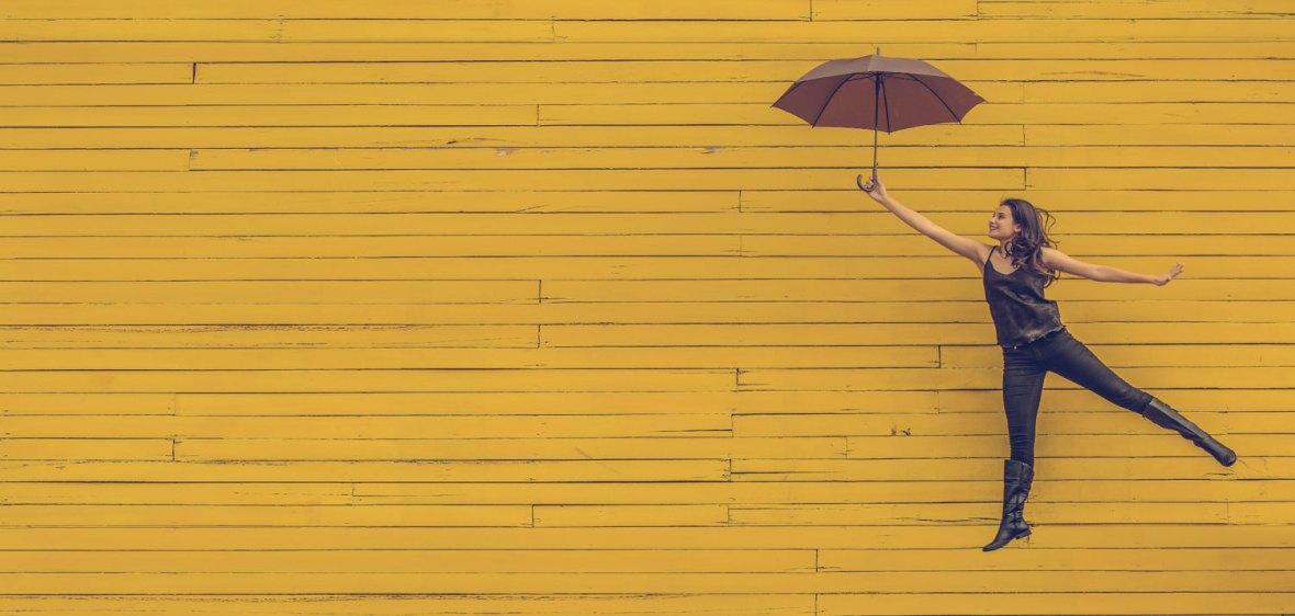image of a flying girl holding an umbrella and smiling against a yellow wooden background