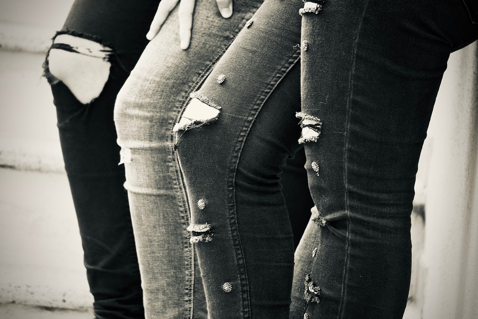 Peoples legs who are wearing jeans which are ripped in parts in a fashionable manner.