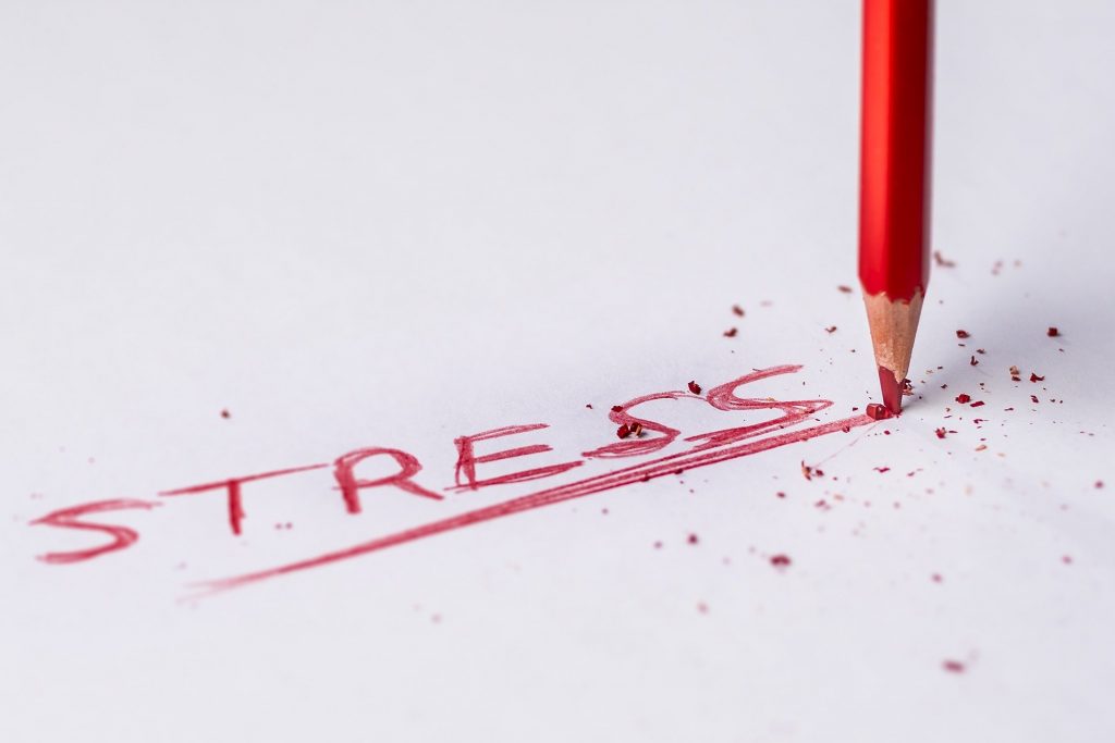 Image of a red pencil writing the word stress on paper.