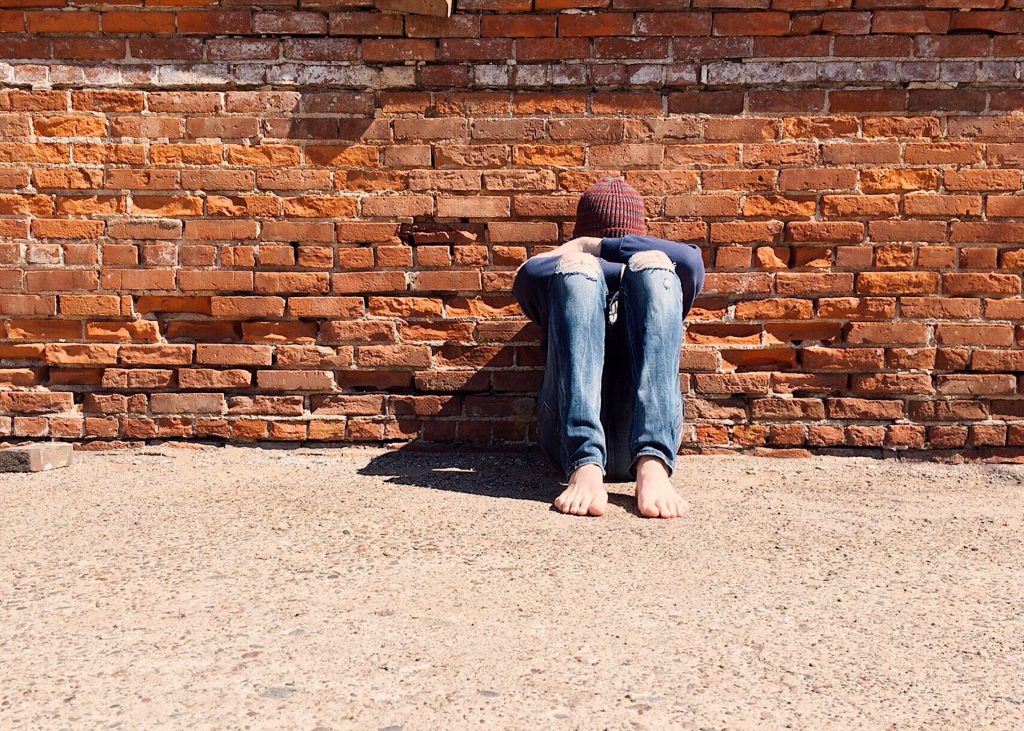 Young person sitting outside alone with head on knees.