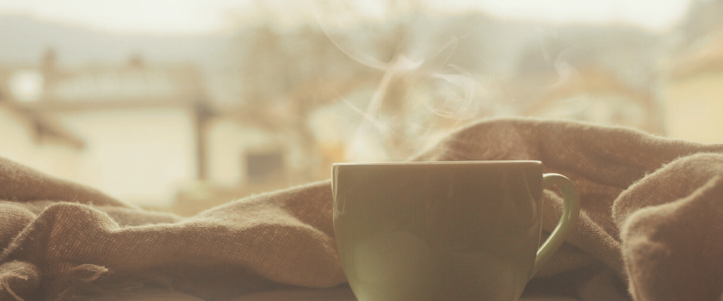 A hot drink, gently steaming, nestled in a blanket.