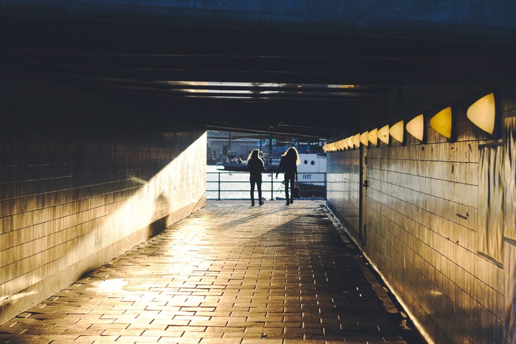 Two people walking through a lit underpass.