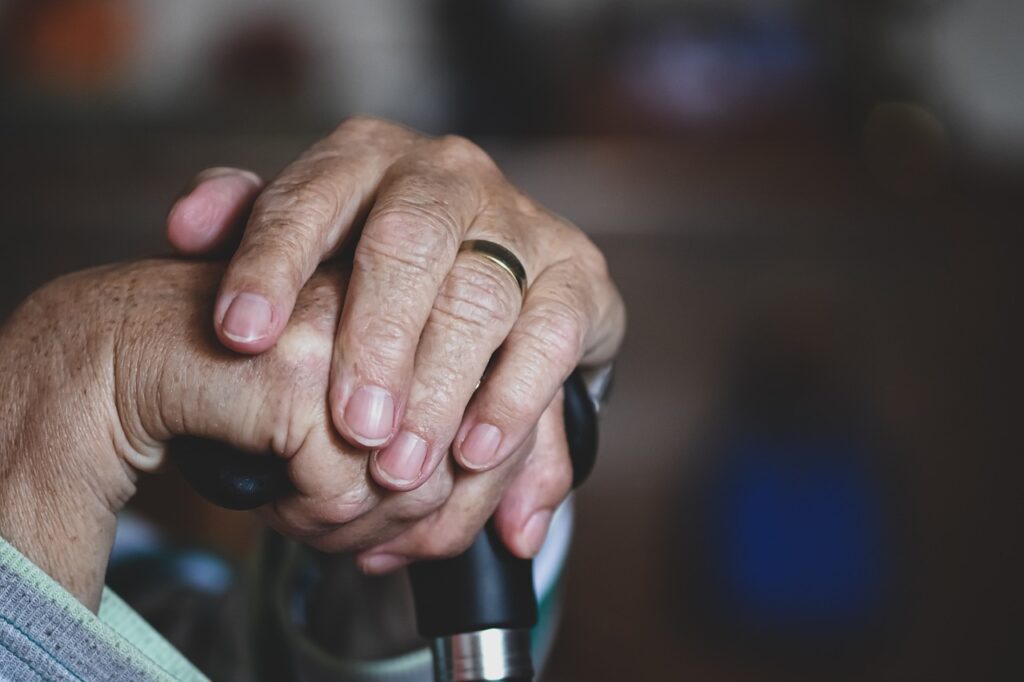 Wrinkled hands holding a walkingstick.