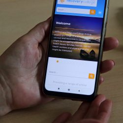Hand holding mobile phone showing the Recovery College Online website